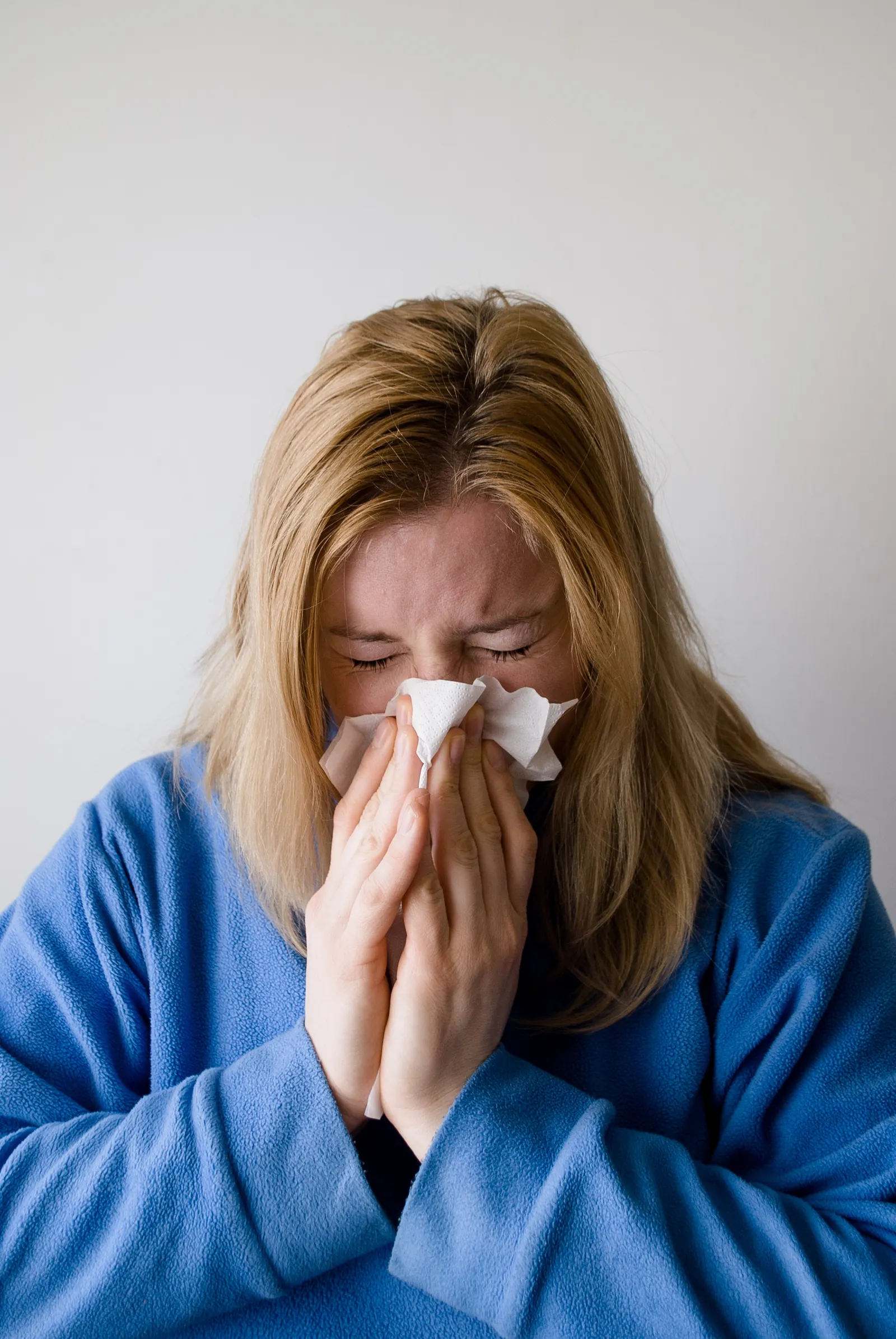 Woman sneezing into a tissue, a common symptom of allergic rhinitis that may require ENT evaluation and allergy testing