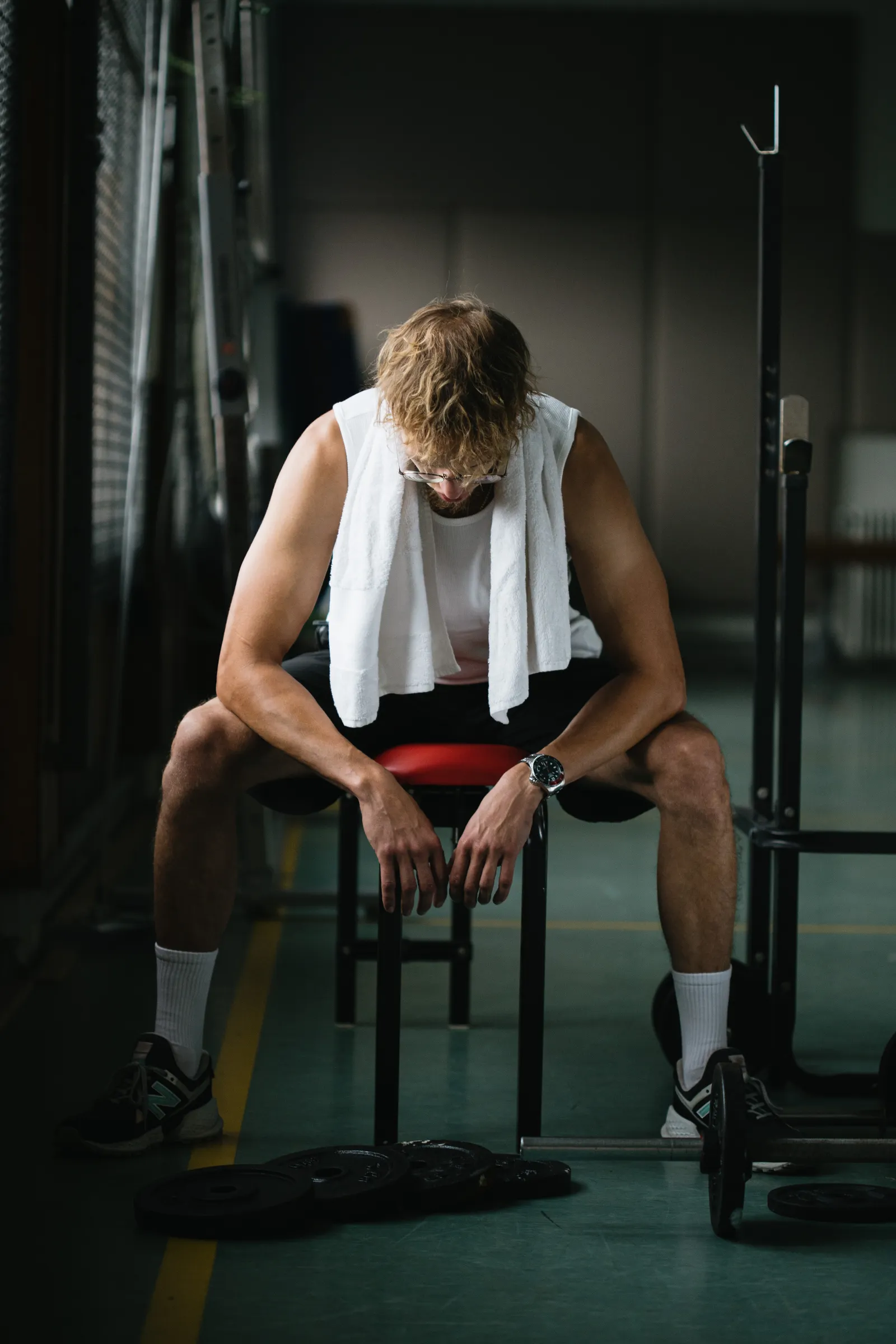 Tired athlete resting on a gym bench after an intense workout, a sign of overtraining that can contribute to hair shedding