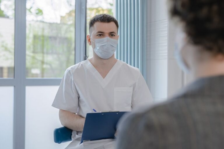 A patient sitting in a clinic room chatting with a doctor who is taking notes
