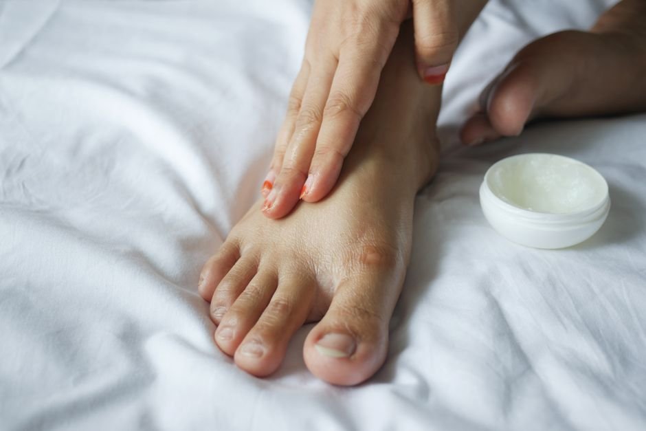 A person in pajamas sitting on the edge of a bed, rubbing moisturizer into the backs of their hands