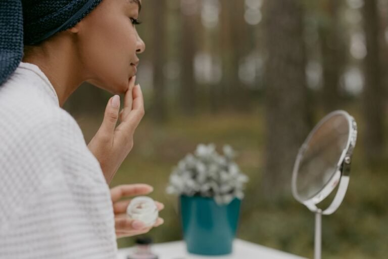 A person applying moisturizer to their face while looking in a bathroom mirror