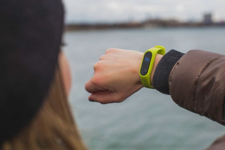 A person standing outdoors in a hoodie glancing at a fitness tracker on their wrist