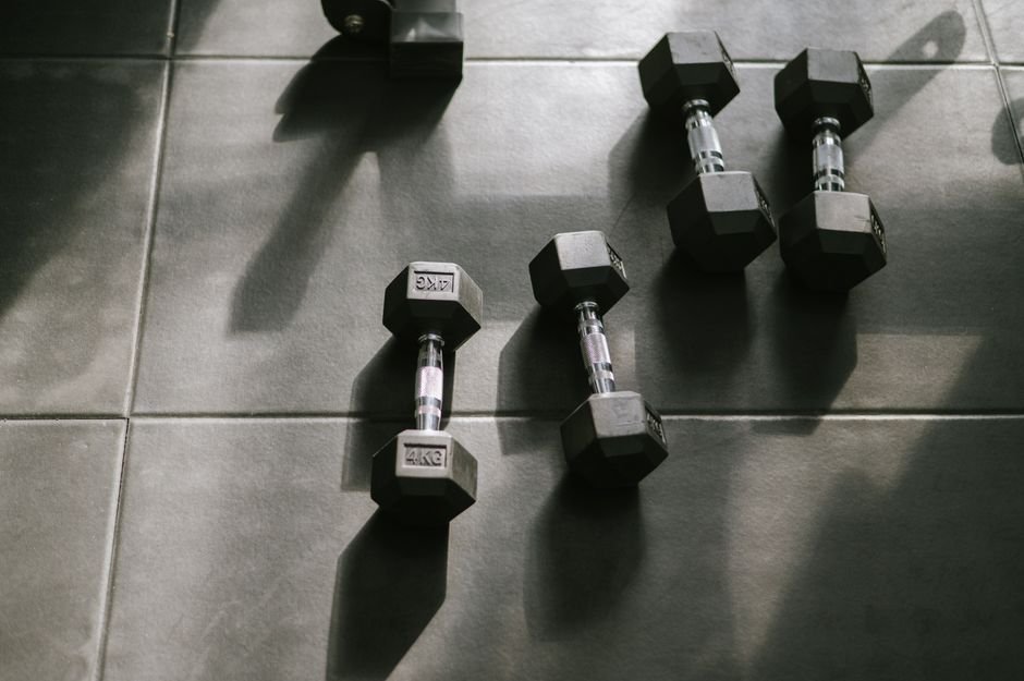 A person kneeling on a gym floor between a set of dumbbells and open floor space