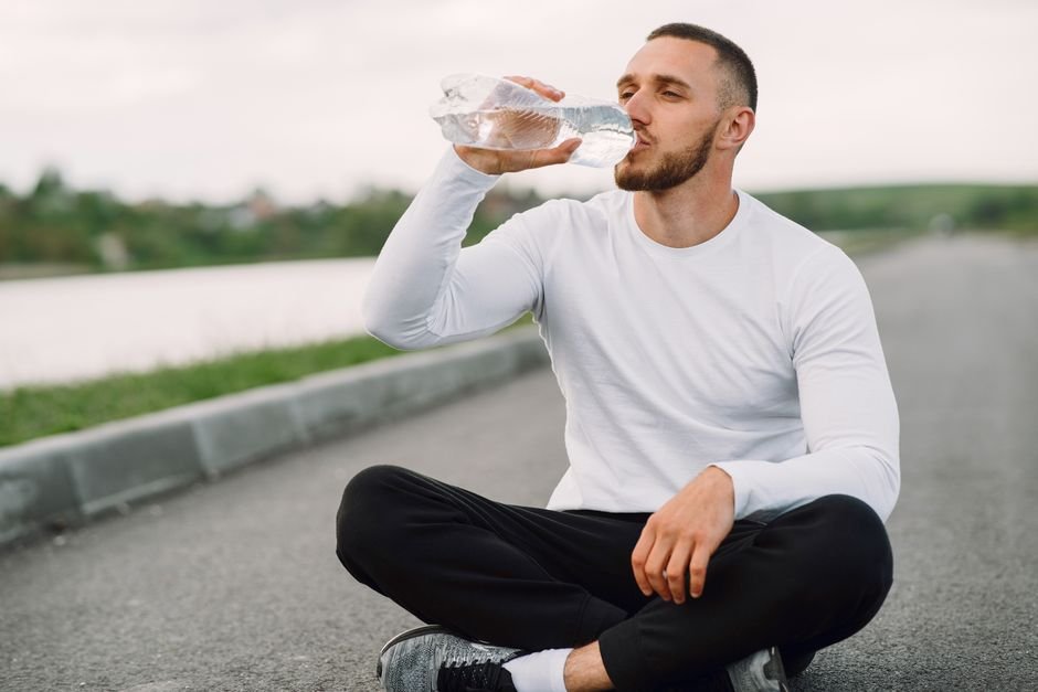A person pausing during a workout to drink water from a reusable bottle