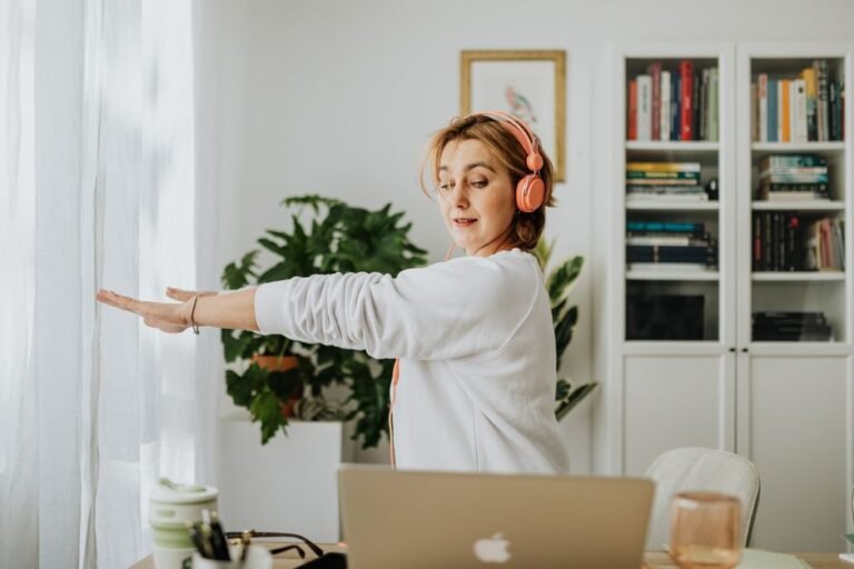 A person standing beside their office desk stretching their arms overhead during a work break