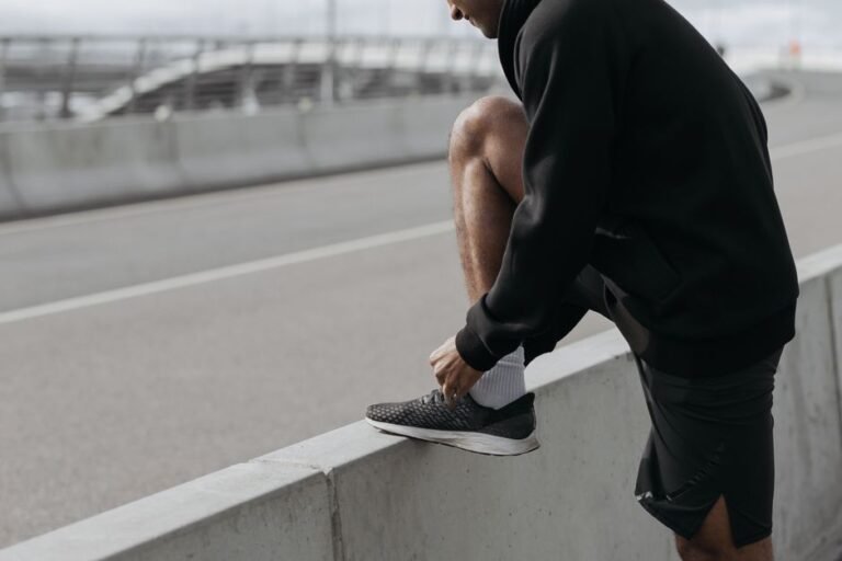 A person sitting on a bed tying their shoes, looking tired but ready to head out