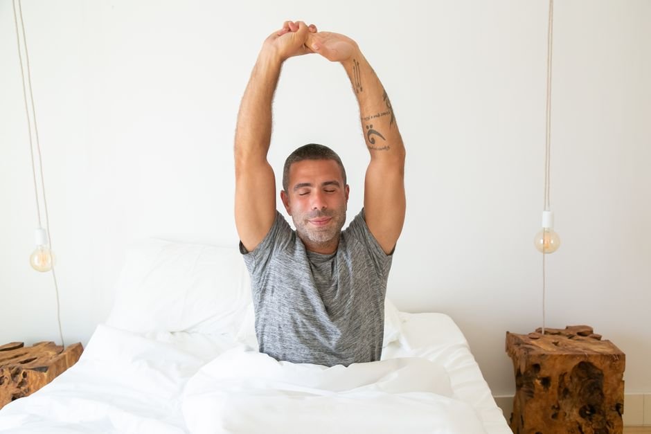 A person waking up and stretching in bed with morning light