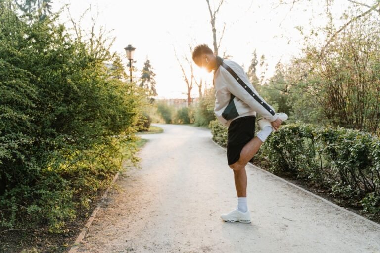 A runner in ordinary workout clothes stretching their calf against a low wall beside a park path