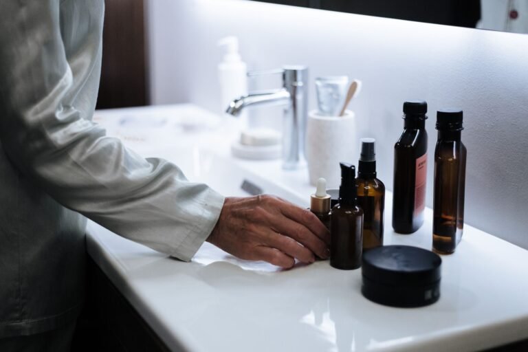 A person's hand reaching for unbranded skincare bottles on a bathroom counter