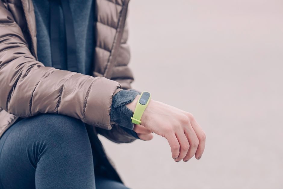 Close view of a person's wrist wearing a simple fitness tracker while they tie a running shoe